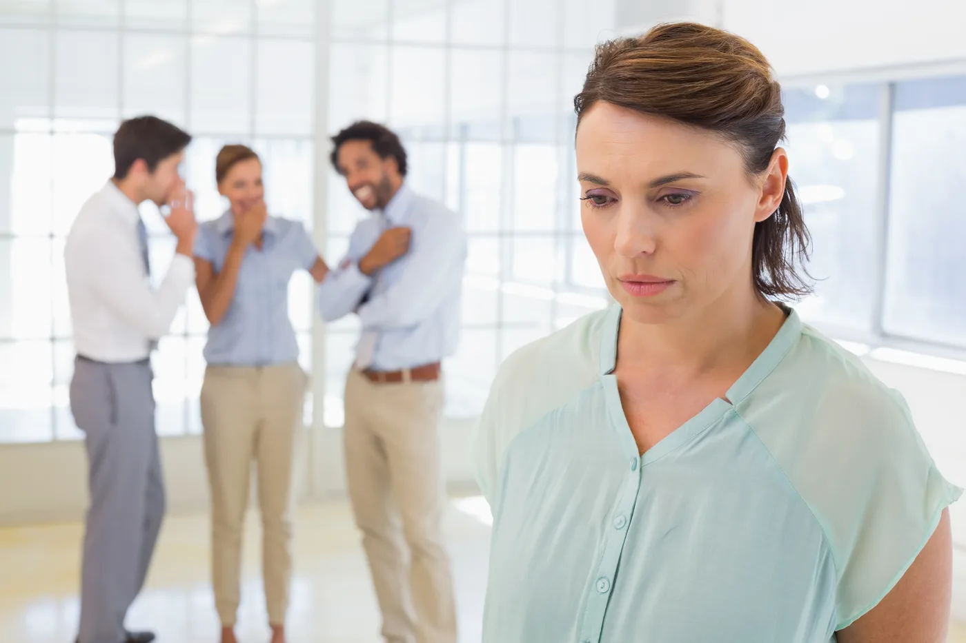 Mulher pensativa em primeiro plano, com pessoas conversando ao fundo